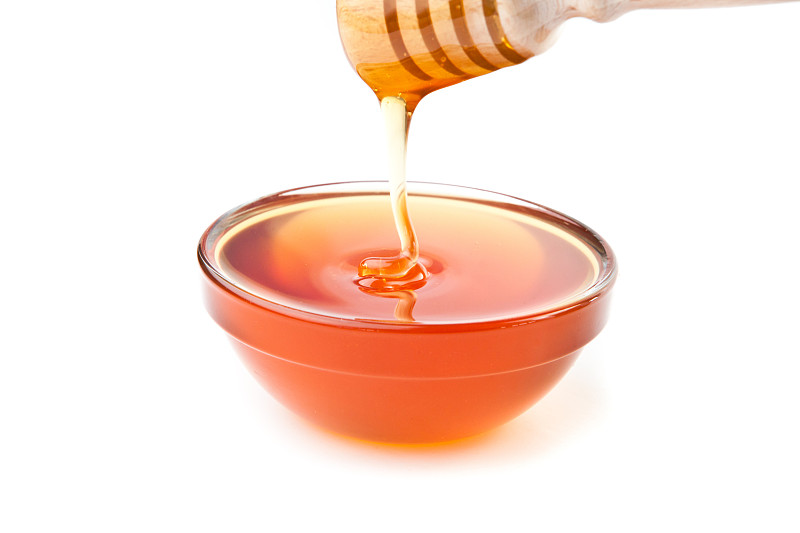 蜂蜜在白色的背景下滴落在蜂蜜碗里图片下载