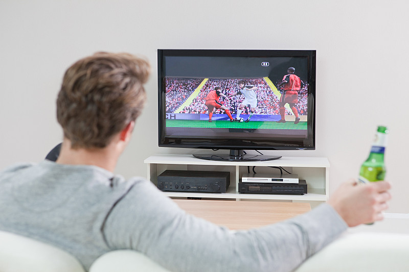年轻人拿着啤酒瓶在电视上看足球比赛图片下载