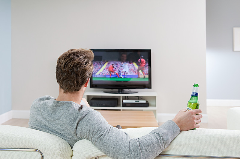 年轻人拿着啤酒瓶在电视上看足球比赛图片下载