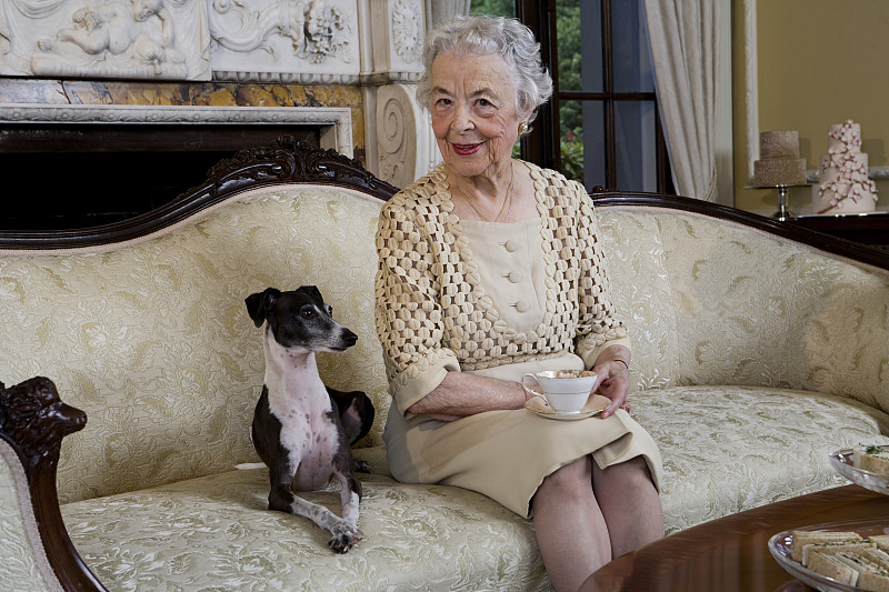 老女人和狗坐在沙发上，面带微笑图片下载