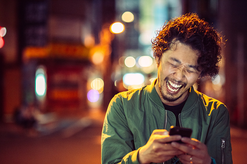 微笑的日本年轻人在城市场景与智能手机图片下载