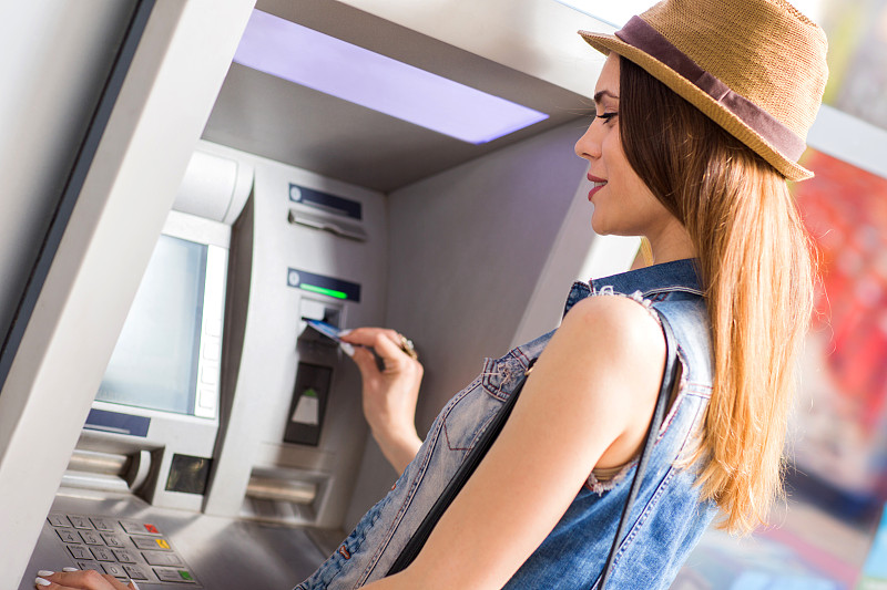 微笑的年轻女子正在自动取款机上取款。图片下载