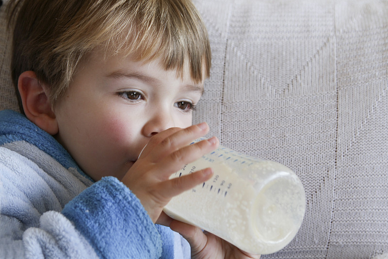 轻松的金发男孩在喂奶瓶喝牛奶图片下载