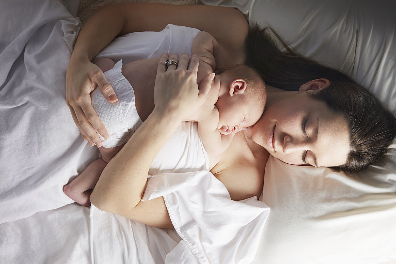 母亲抱着新生婴儿睡在床上图片下载