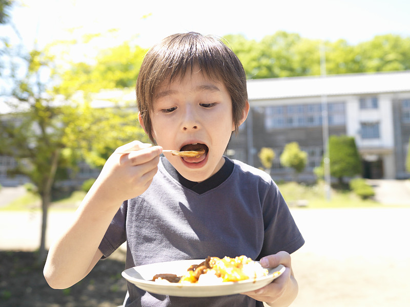 男孩(6-7岁)在学校操场上吃咖喱图片下载