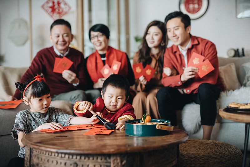三代快乐的亚洲家庭庆祝农历新年，手里拿着“红包”，小朋友在前面练习书法，写“中国新年吉祥信息”图片下载