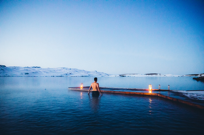 男人正在温泉池里洗澡，可以看到冰岛的雪山和冰湖图片素材
