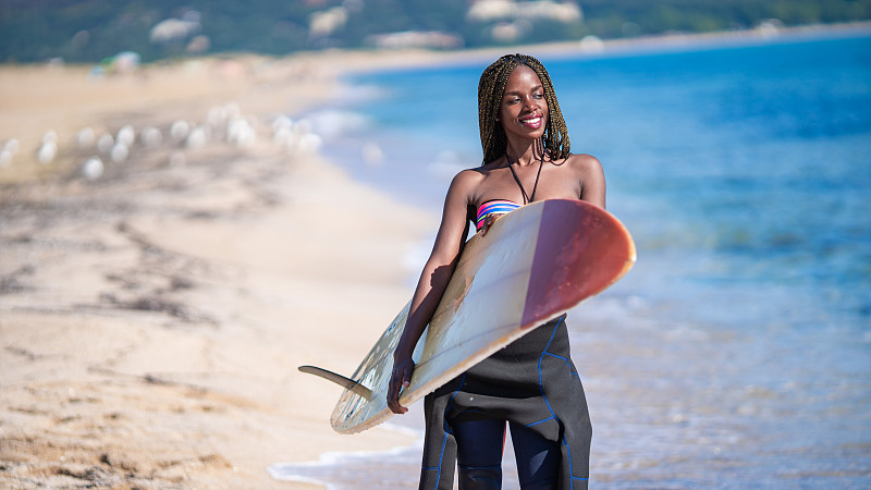 非洲妇女拿着冲浪板在海滩上行走图片下载