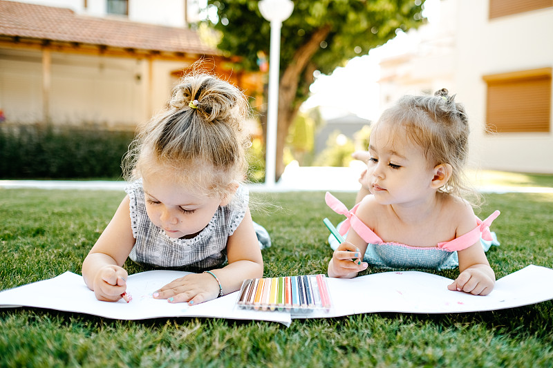 小女孩们在户外草地上的画纸上画画图片下载