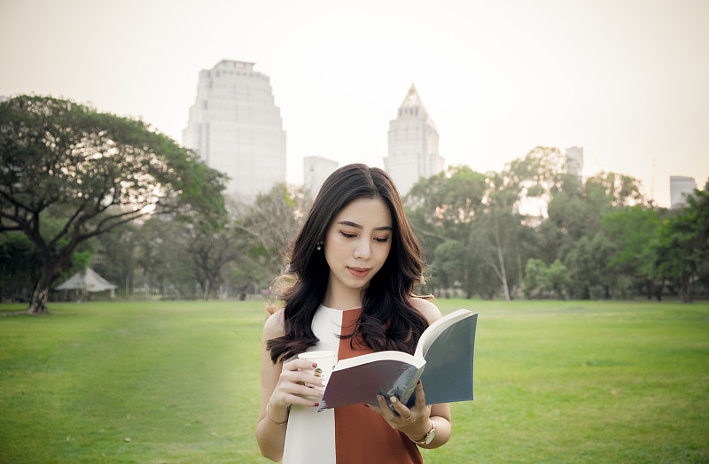 年轻女子放松在城市的公共公园与书和一杯咖啡图片素材
