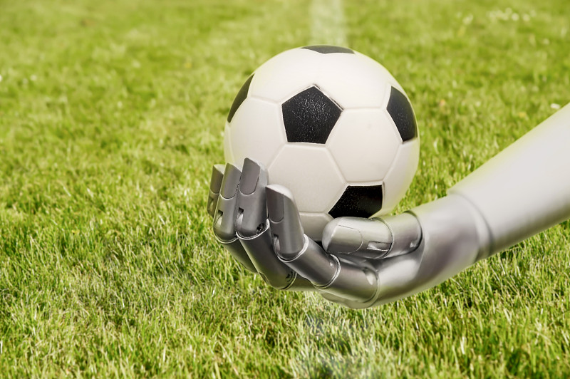 机器人手臂伸向足球。用机器踢足球。机器人手臂和足球场。图片素材