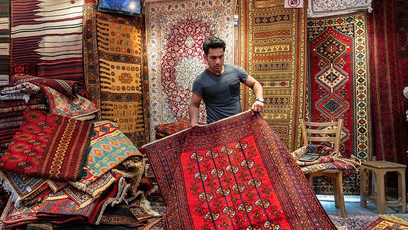 伊朗伊斯法罕的一家地毯商店里，年轻的伊朗地毯售货员向游客展示波斯地毯图片下载