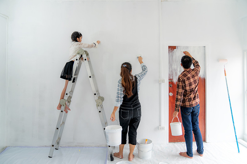 幸福的亚洲家庭与父亲，母亲和女儿在粉刷粉刷白色的墙壁在他们的新房子。家庭生活爱情关系，还是新房活动概念图片下载