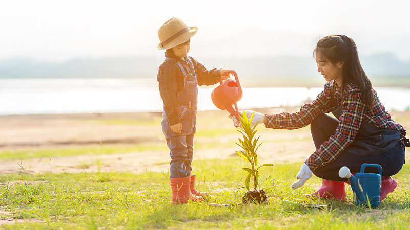 亚洲家庭妈妈和孩子在大自然的春天在户外种植树苗，以减少全球变暖的生长特征，爱护自然地球。人族河流背景图片素材