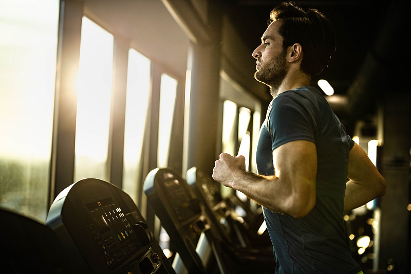 积极的男性运动员在健身房的跑步机上慢跑。图片素材