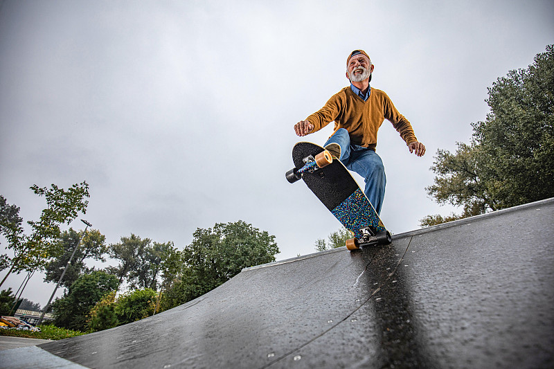 下图是快乐的老人在公园的斜坡上玩滑板。图片素材