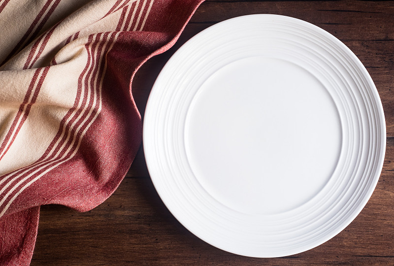在旧的木制棕色背景上，空的餐巾白色盘子，俯视图。图像与复制空间。厨房桌子与毛巾和一个盘顶视图与复印空间。图片下载