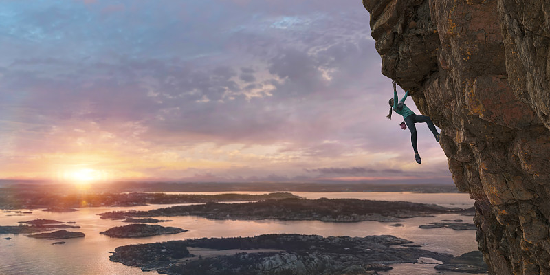 女性自由攀登者在黎明攀登陡峭的海岸岩石面图片下载