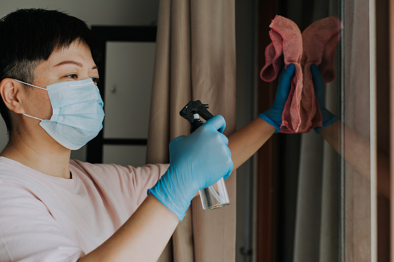 一名亚洲华人女性戴着口罩，双手戴着乳胶手套擦拭玻璃窗户图片下载