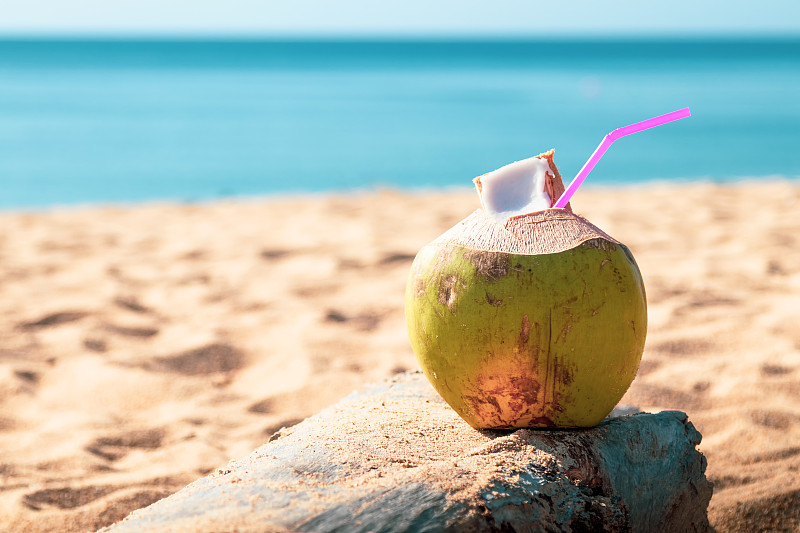 甜美的绿色椰子水和饮用稻草在泰国普吉岛的沙滩上。图片素材