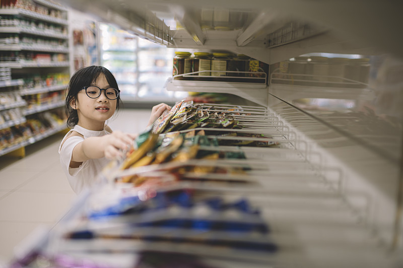 一个亚洲的中国小女孩从货架上挑选商品，然后在超市里拿起其中的一个图片素材