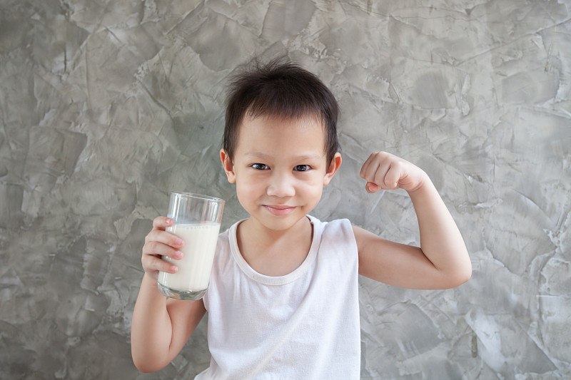 可爱的亚洲男孩拿着牛奶杯，在家里做着强有力的手势图片下载