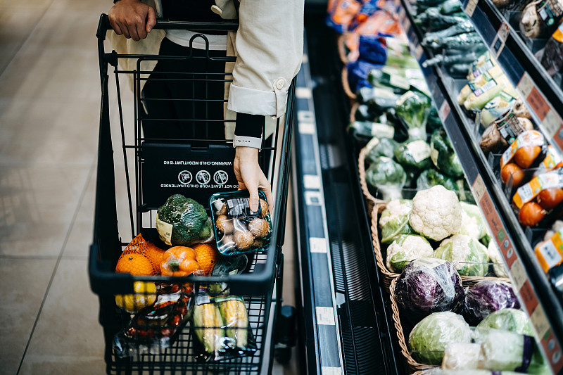 近距离的女人的手在超市购买新鲜的食品杂货，并把各种有机蔬菜在购物车图片素材
