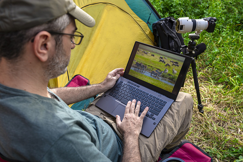 摄影师在帐篷里用笔记本电脑工作。图片下载
