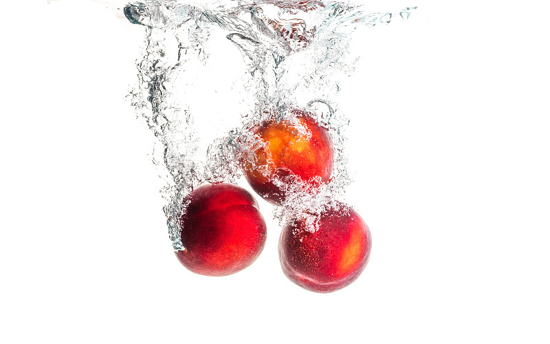 油桃水果溅入水和下沉与空气泡孤立在白色背景。图片素材
