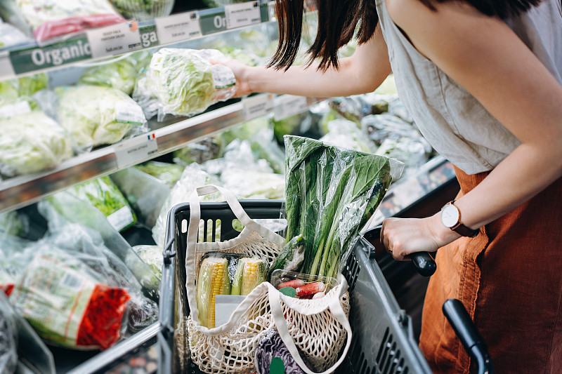裁剪的镜头年轻的亚洲妇女在超市购买新鲜的有机食品杂货，并把各种水果和蔬菜放入棉花网生态袋在购物车。“零浪费”的概念图片素材