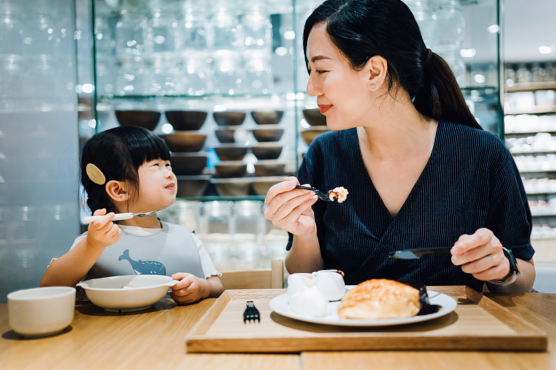 年轻的亚洲母亲和可爱的小女儿在咖啡厅享用甜点。他们互相看着，开心地笑着图片下载