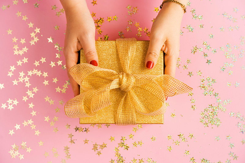 女人的手拿着一个绿色的礼品盒与黄色缎带在粉红色的背景图片素材