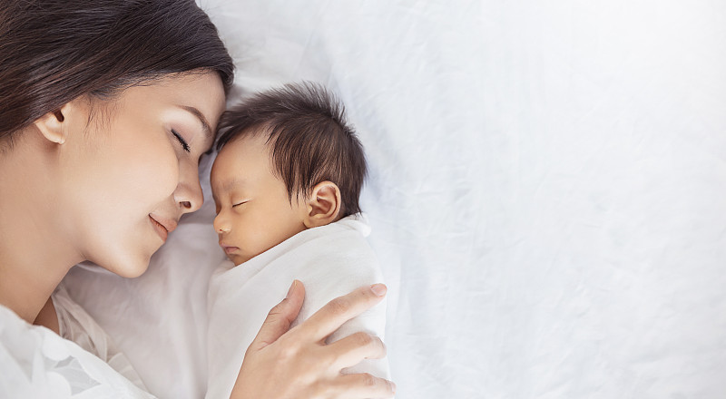 近距离的美丽年轻的亚洲或高加索母亲女孩亲吻她的健康的新生婴儿睡在床上复制空间。健康医疗爱亚女性生活方式母亲节理念图片下载