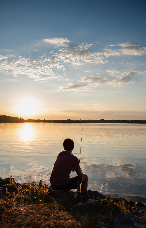 Adolescent boy fishing on shore of lake at sunset in Ontario, Canada.图片素材