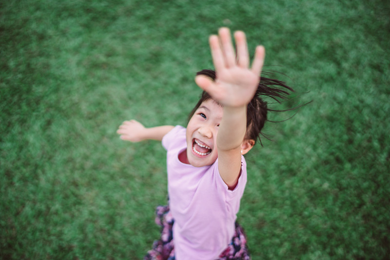 可爱的小女孩一只手伸向天空，在公园的草坪上快乐地玩耍图片下载