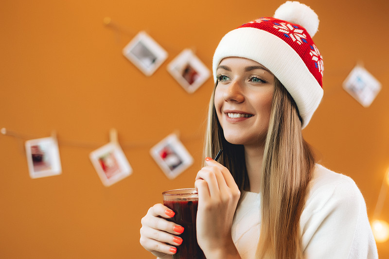 圣诞女肖像配酒，女人配热酒戴圣诞老人帽。这个人正在喝酒精饮料。圣诞节的气氛。新年摄影。图片下载
