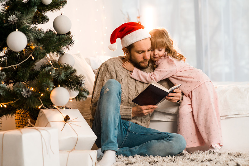 戴圣诞帽的父亲给他心爱的女儿读童话故事图片下载