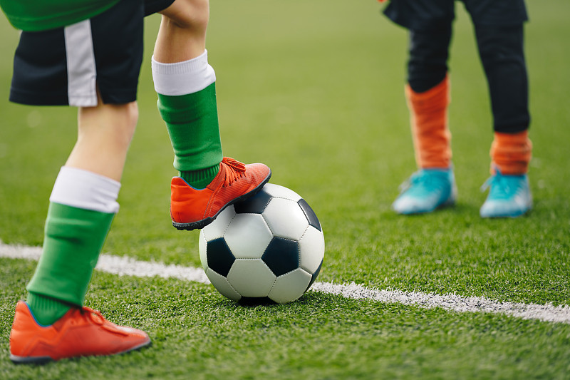 足球运动员腿上的经典球的特写图像。在一场比赛中，足球场和球员的足球背景。穿着运动鞋的男孩在踢球。图片下载