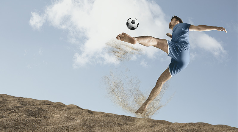 在一个阳光明媚的日子里，足球运动员们在沙滩上拼命地踢沙滩足球图片下载