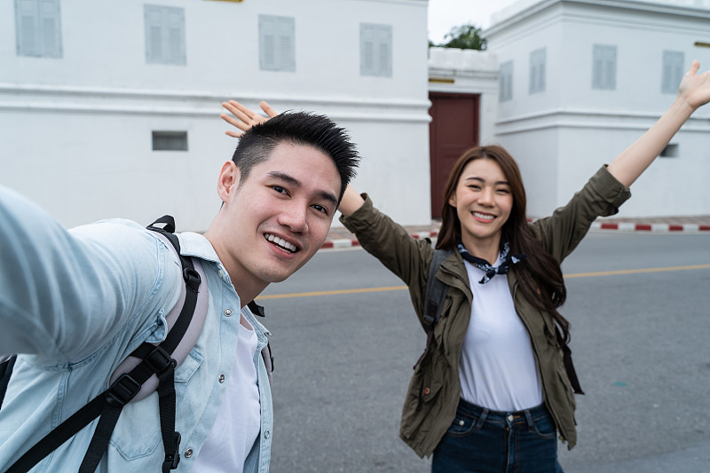 亚洲背包客夫妇用手机自拍，在城市里拍照。有魅力的男女游客在街上旅行，用智能手机录视频，在泰国度假旅行。图片下载