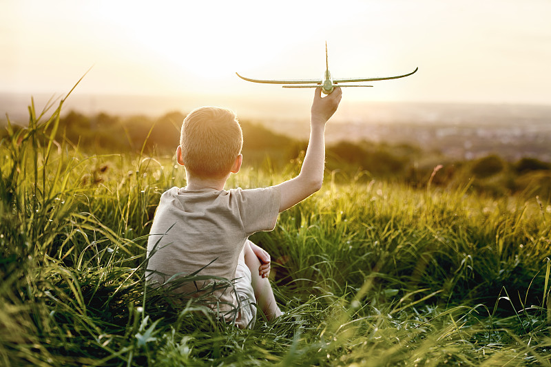 小男孩拿着玩具飞机坐在草地上图片下载