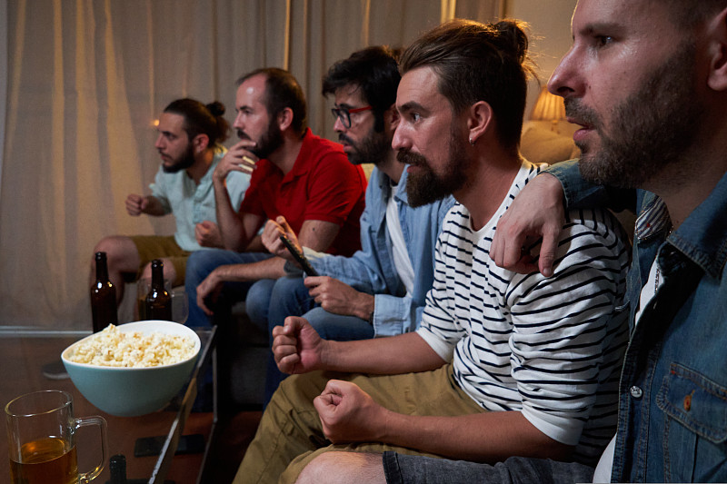 一群男性聚精会神地坐在客厅的沙发上看世界杯足球赛。图片下载