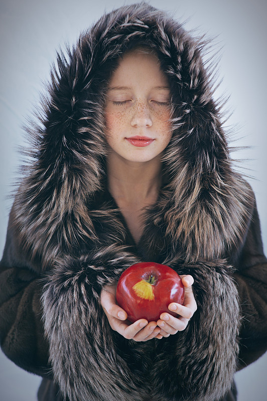 小女孩，长着雀斑，穿着皮衣，闭着眼睛，手里拿着一个红苹果图片下载