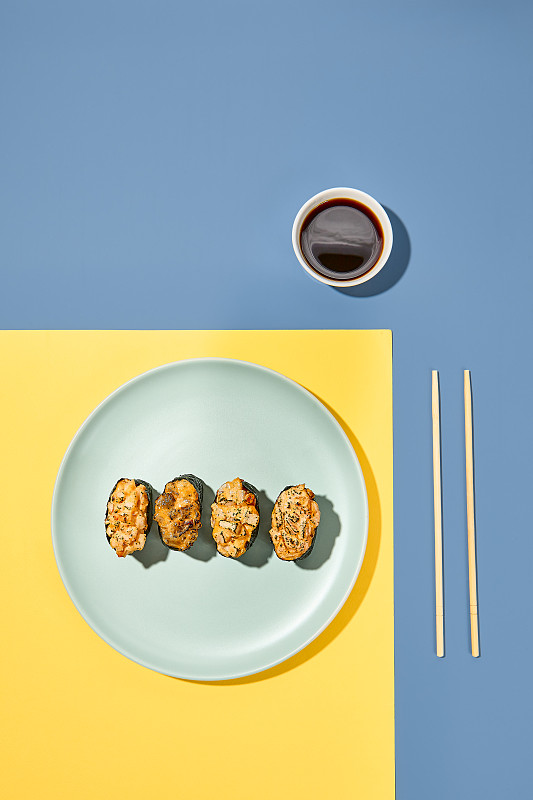 用筷子和酱油在彩色背景的盘子里摆上刚坎寿司。日本菜的最低成分。时尚的概念。Gunkan设置在充满活力的黄色和蓝色背景华丽的食物图片下载