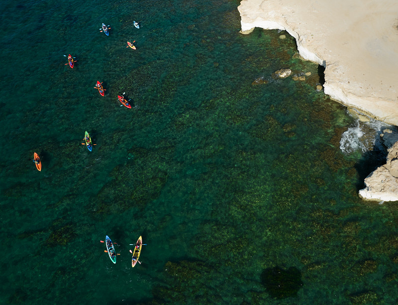 一群人在白色岩石海岸线附近的海里划皮艇。图片下载