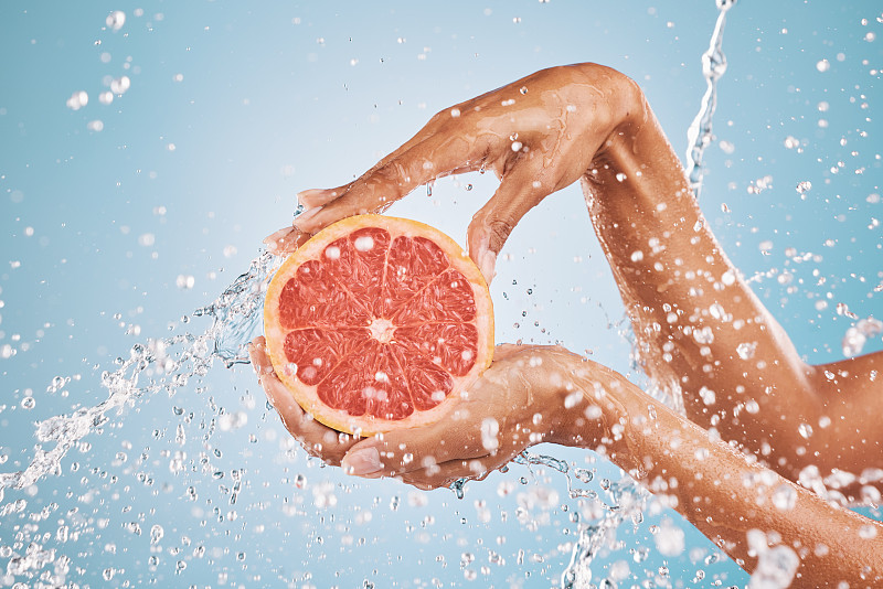手部、水泼柚子美容护肤为维生素c营养，柑橘保健治疗和自然养生。健康的皮肤卫生，广告补水和蓝色的工作室背景图片下载