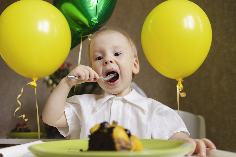 男孩在家里吃蛋糕，后面有气球图片下载