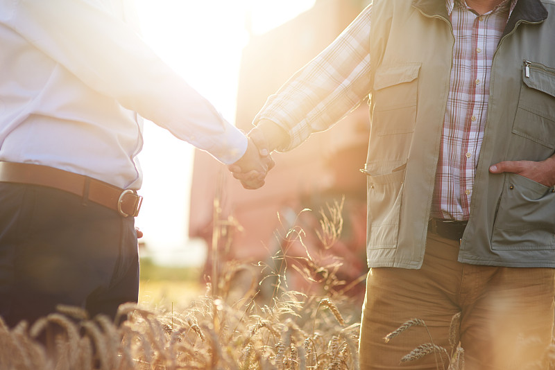 Cropped view of farmer and businessman in wheat field shaking hands图片素材