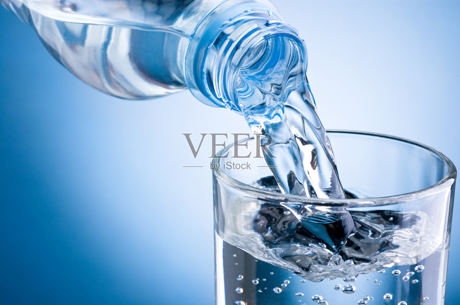 将水从瓶子倒入蓝色背景的玻璃杯中照片摄影图片