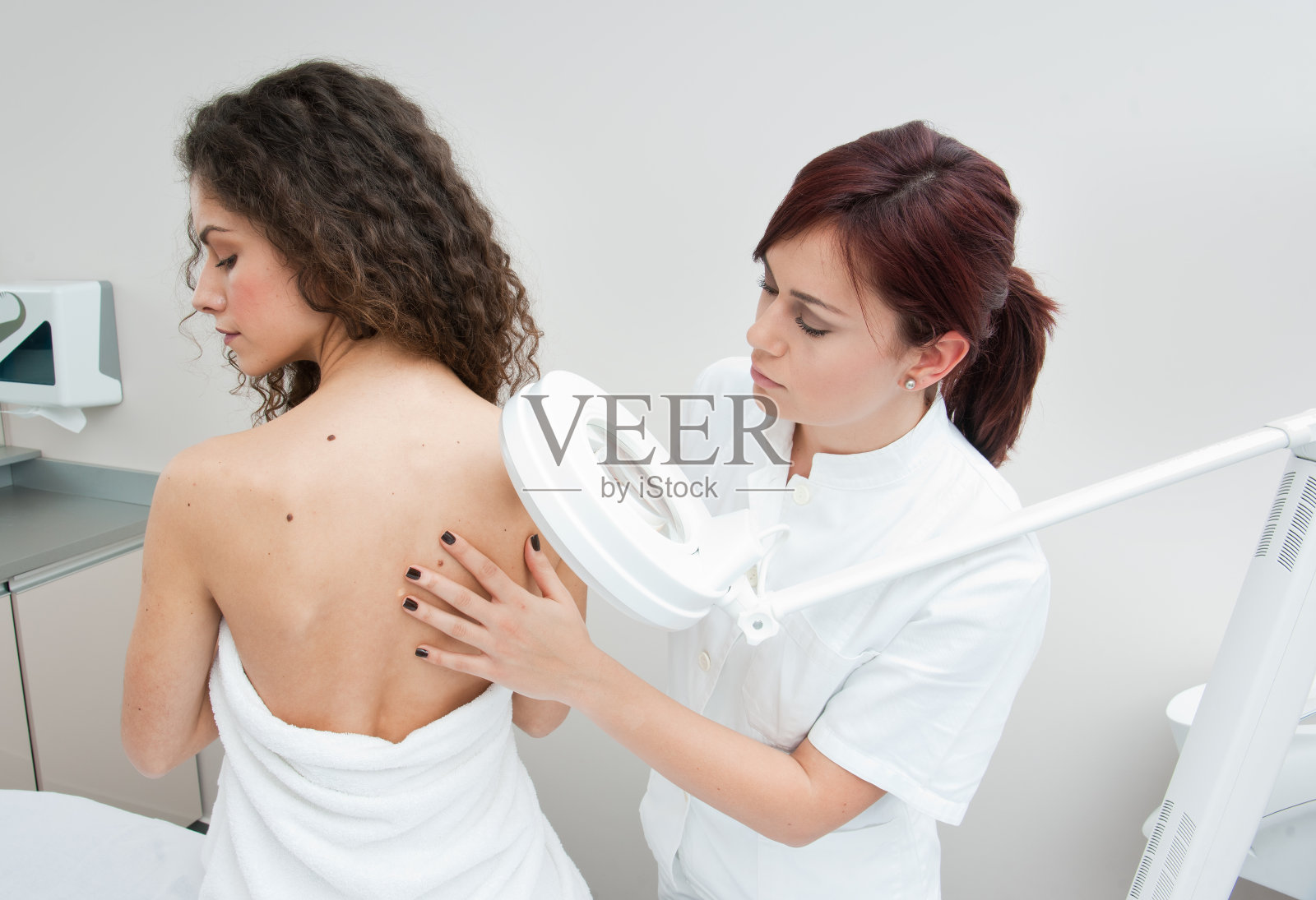 一位皮肤科医生正在检查一位年轻女士的背部照片摄影图片